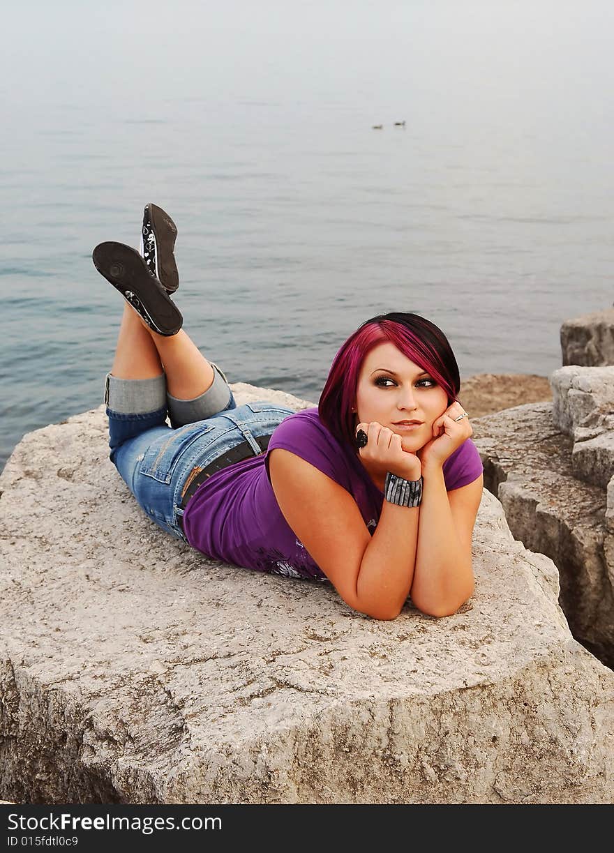 An red hair girl in jeans lying on the shore of lake Ontario at sunset. An red hair girl in jeans lying on the shore of lake Ontario at sunset.