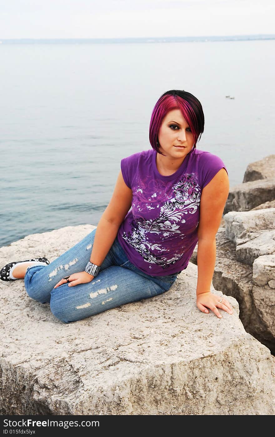 An red hair girl in jeans sitting on the shore of lake Ontario at sunset. An red hair girl in jeans sitting on the shore of lake Ontario at sunset.