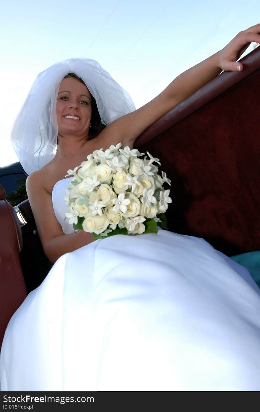 A beautiful smiling bride holding a white rose bouquet sitting in the back seat of a convertible. A beautiful smiling bride holding a white rose bouquet sitting in the back seat of a convertible