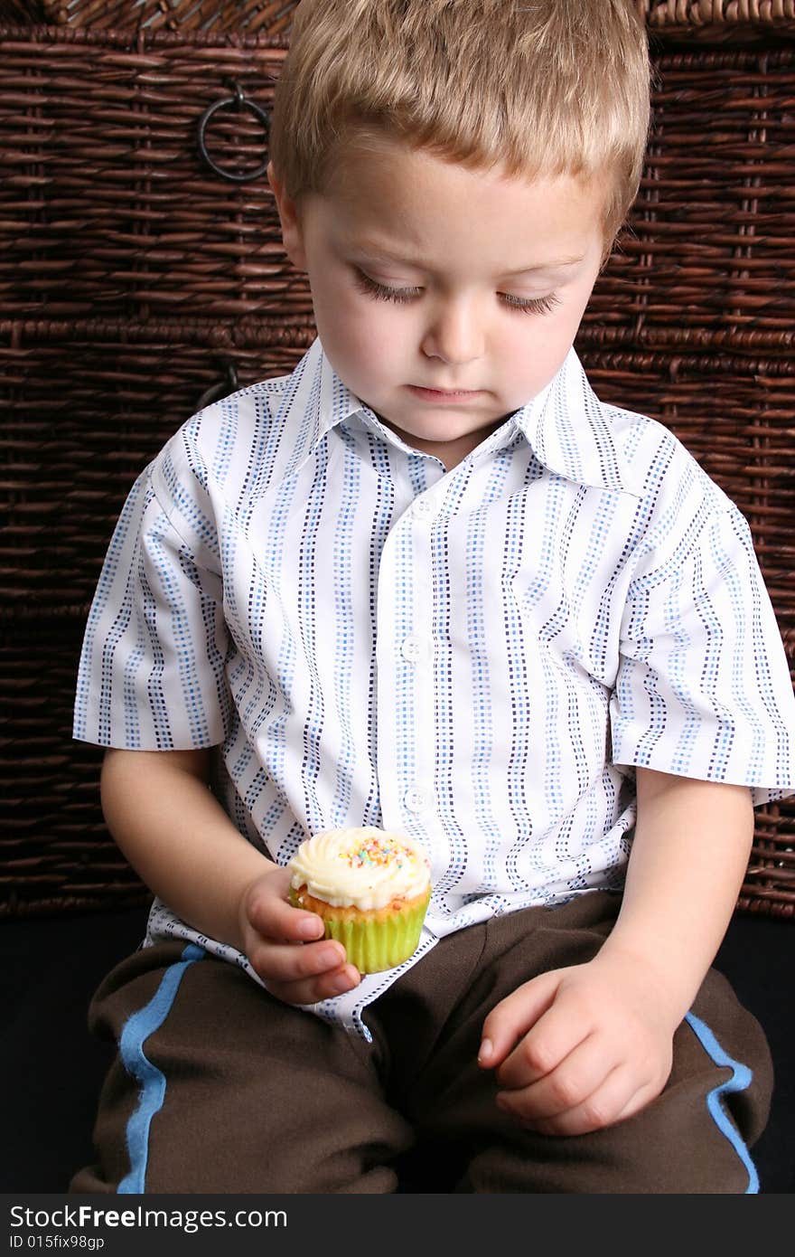 Beuatiful Blond toddler looking down at his cupcake. Beuatiful Blond toddler looking down at his cupcake