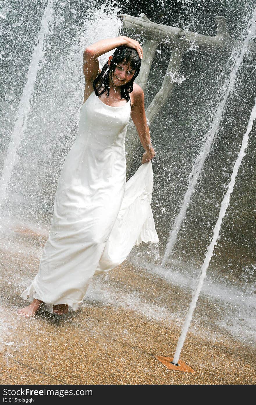 Beautiful young bride playing in a waterfall on her wedding day.