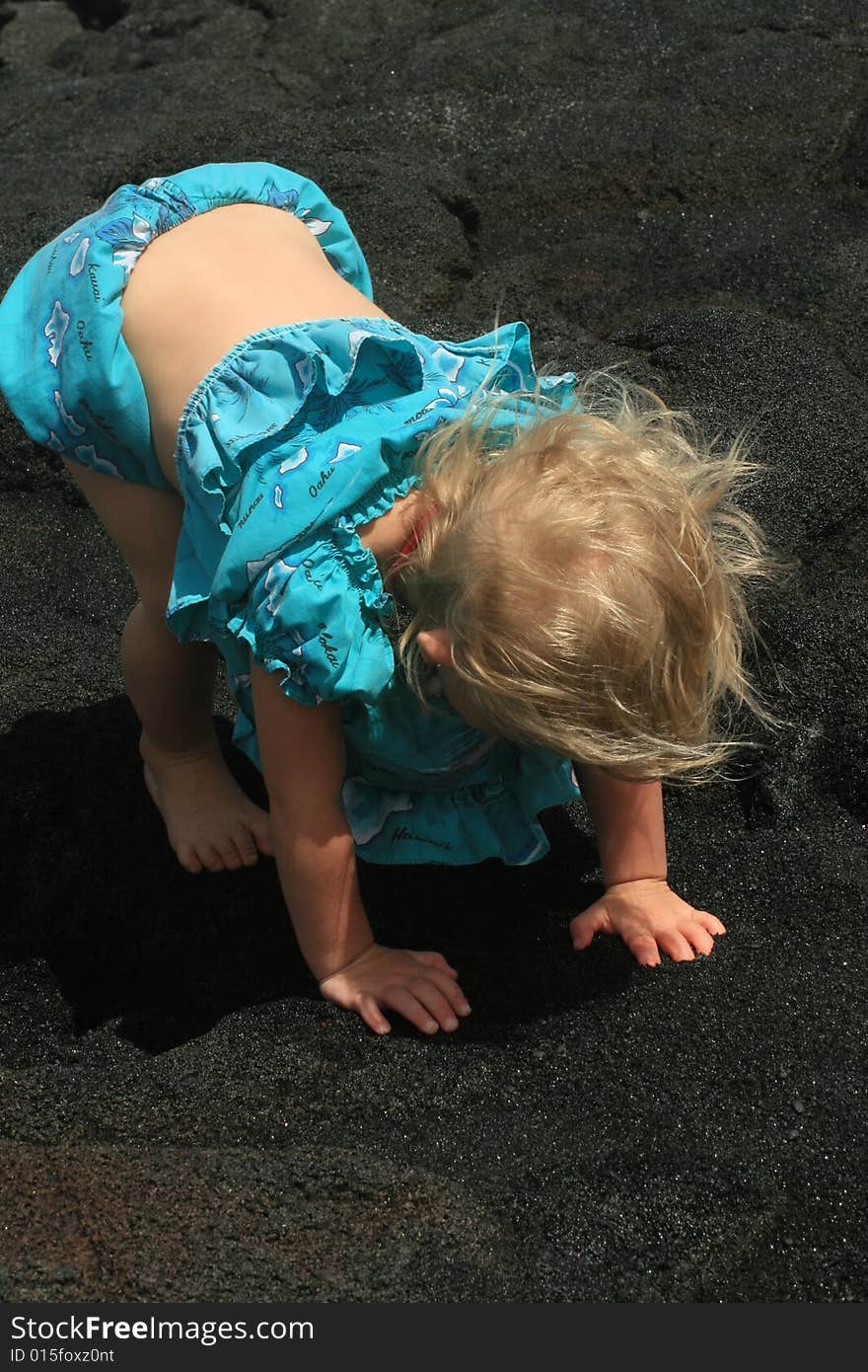 Little girl playing in black sand with her hawaii dress on. Little girl playing in black sand with her hawaii dress on