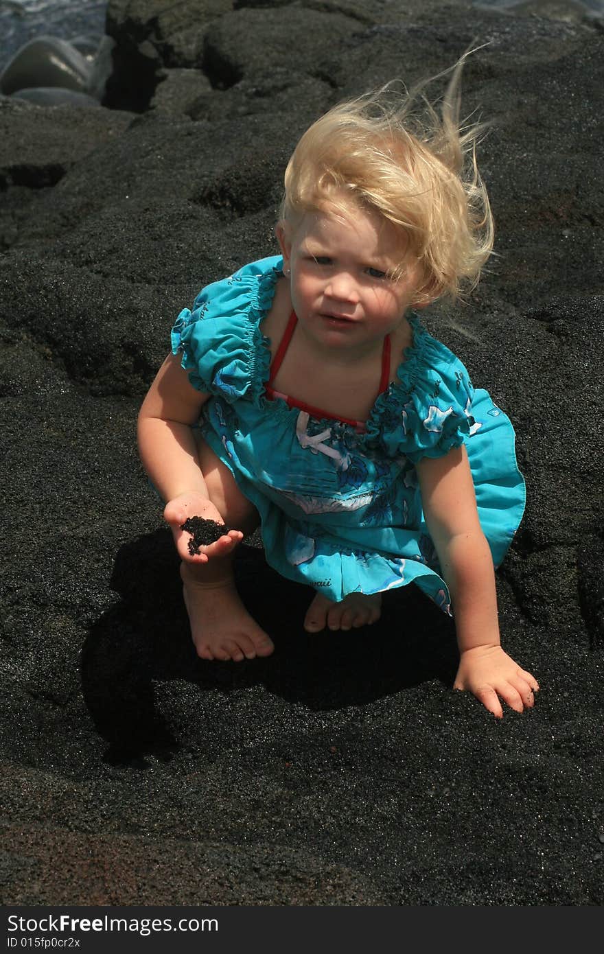 Blonde little girl with black sand in her right hand as the wind blows her hair