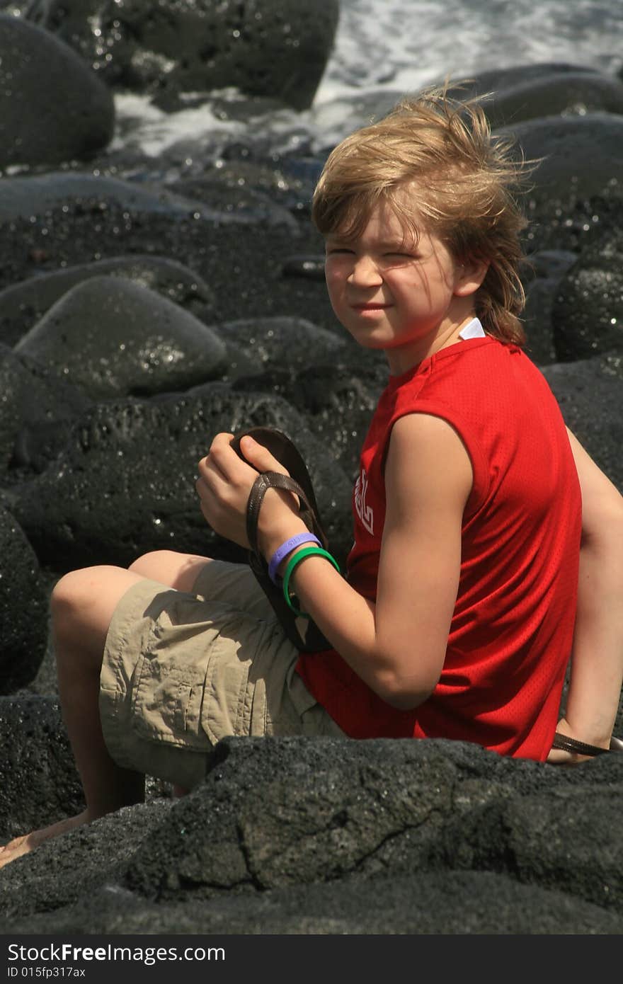 Young boy sitting on lava while playing in black sand. Young boy sitting on lava while playing in black sand