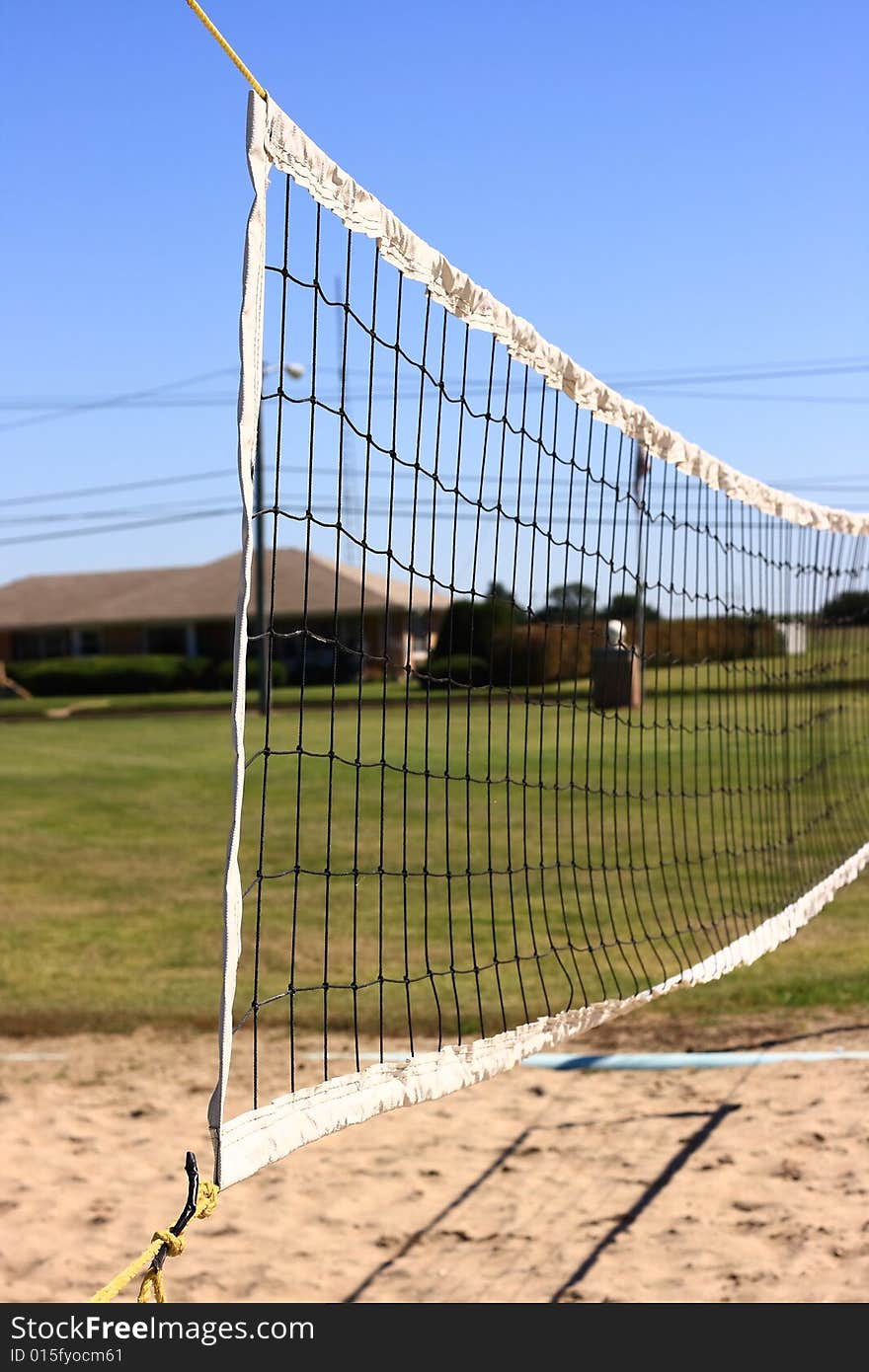 A volleyball net hangs over the sand in the middle of a green city park. A volleyball net hangs over the sand in the middle of a green city park.