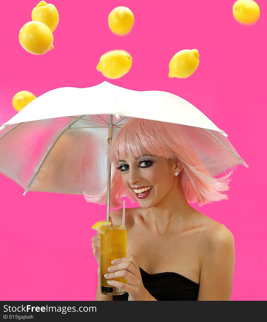 Beautiful smiling girl holding a glass of lemonade and an umbrella over her head as lemons rain down on her from the sky.  Isolated on a pink background. Beautiful smiling girl holding a glass of lemonade and an umbrella over her head as lemons rain down on her from the sky.  Isolated on a pink background.