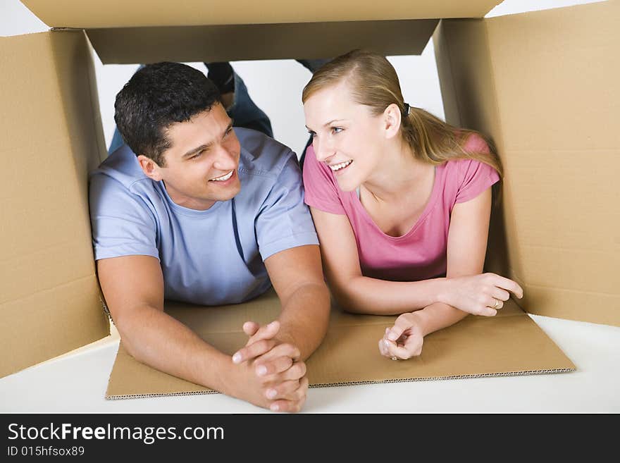 Young smiling couple lying in cardboard box and talking. Front view. Young smiling couple lying in cardboard box and talking. Front view.