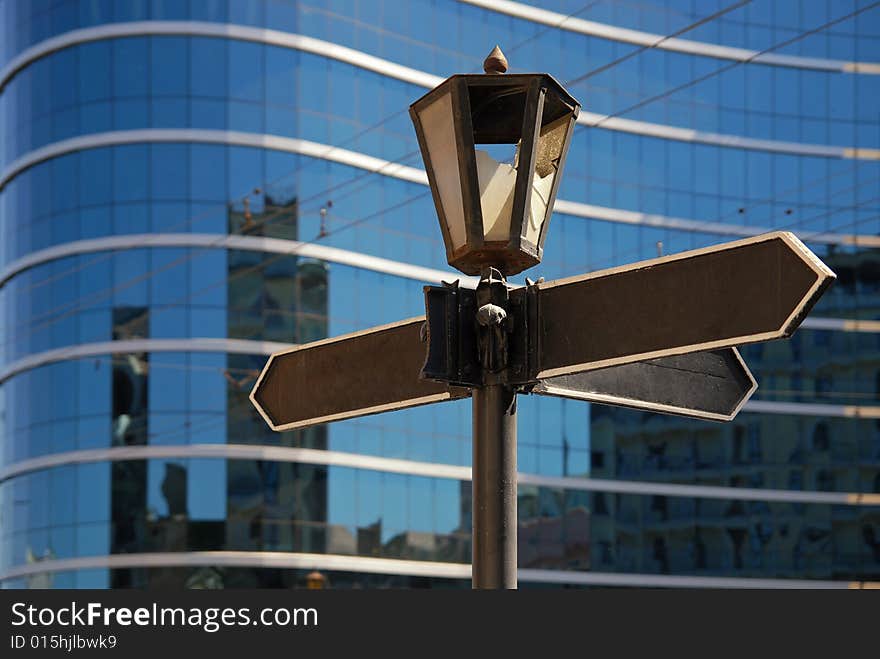 Blank signpost with ancient lamp against business building