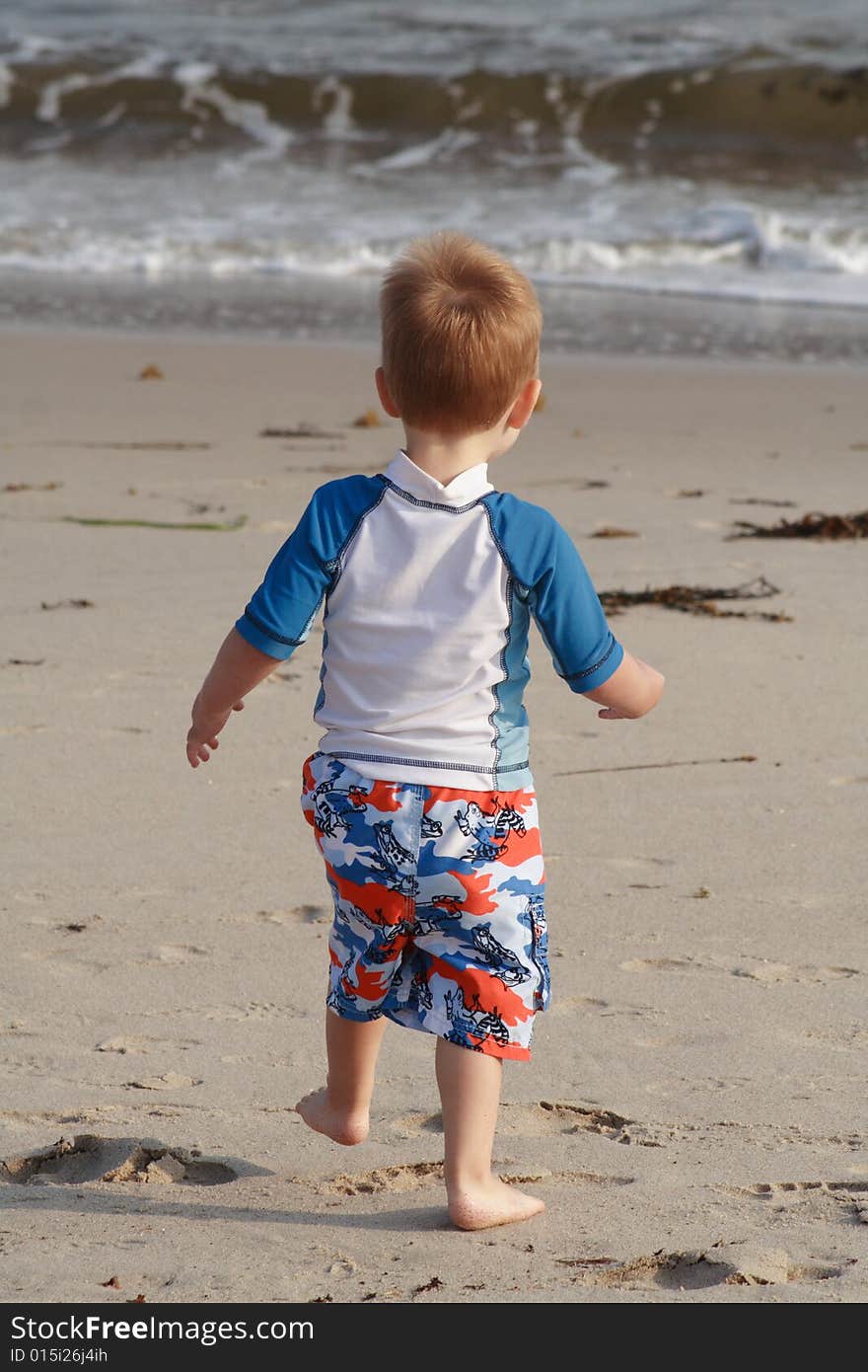 A toddler boy running towards the water on a sandy beach. A toddler boy running towards the water on a sandy beach.