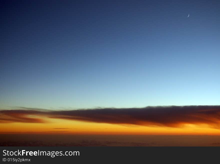 crescent-shaped moon at dusk above the cloud