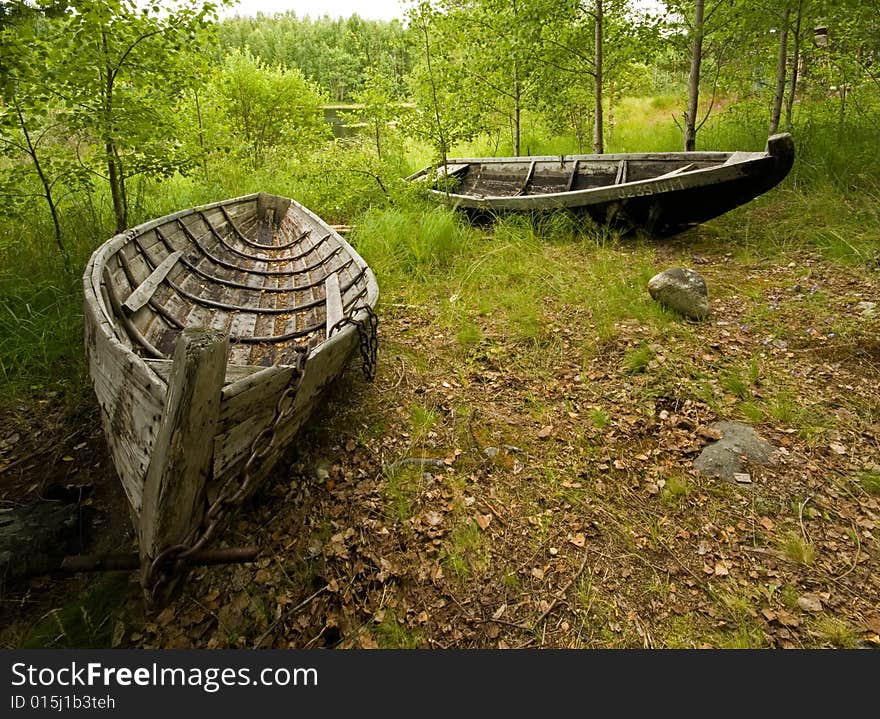 Two old wooden boats lie close to the bank of a lake. Two old wooden boats lie close to the bank of a lake