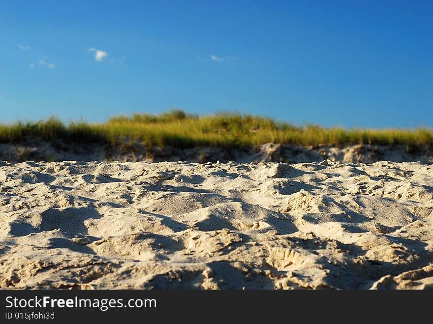 This is a shot of a sandy beach looking towards a grassy knoll and blue sky with small plumes of cloud.