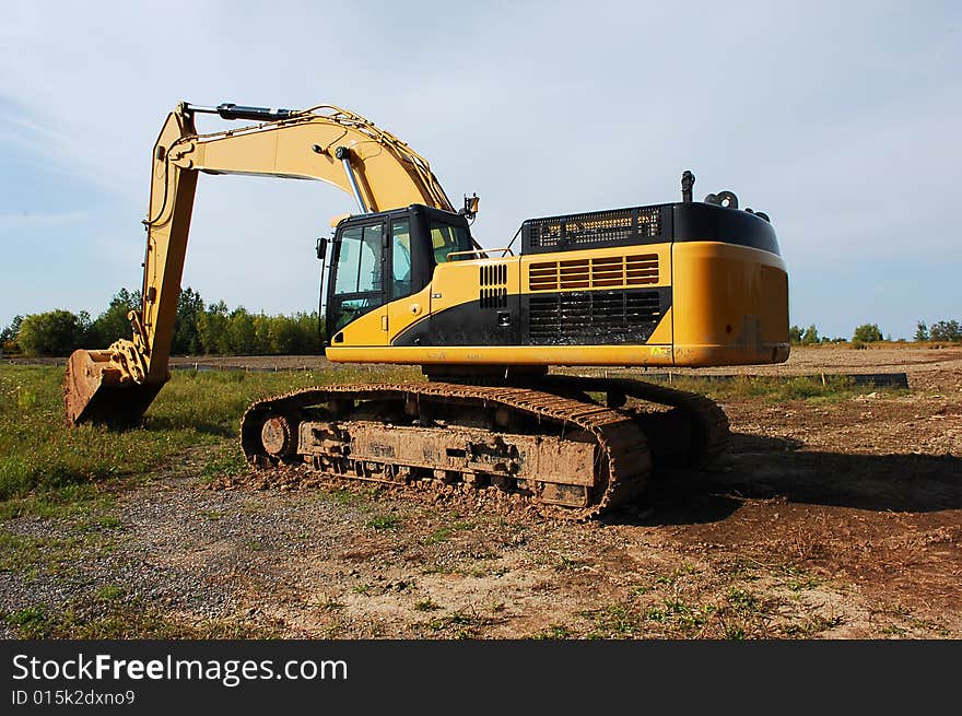 An yellow heavy excavator sitting on an field to begin construction of an industrial site. An yellow heavy excavator sitting on an field to begin construction of an industrial site.