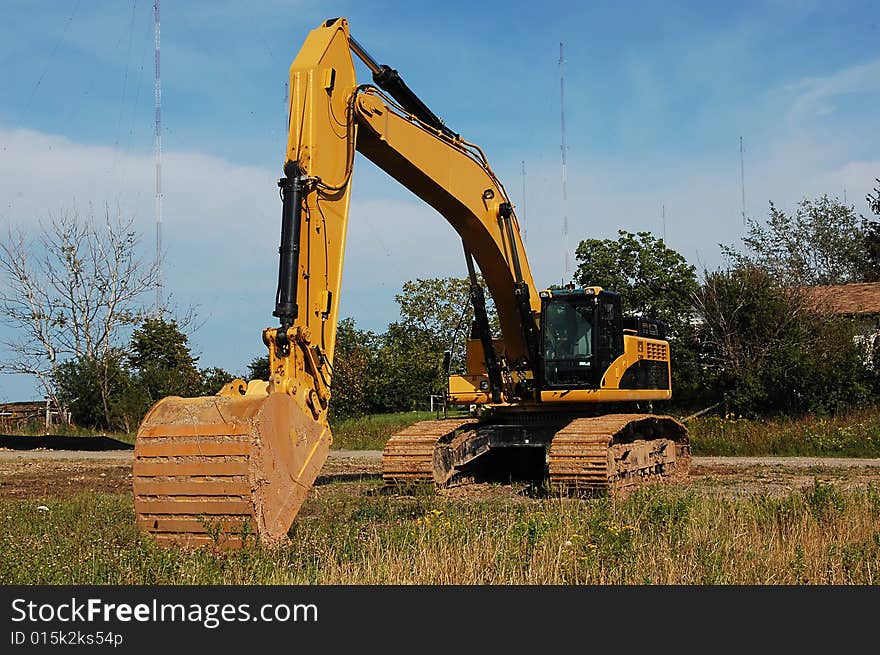 An yellow heavy excavator sitting on an field to begin construction of an industrial site. An yellow heavy excavator sitting on an field to begin construction of an industrial site.