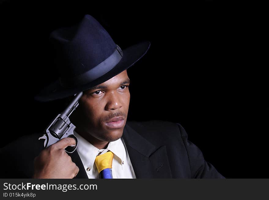 Young African American man in a hat and suit with gun to his head isolated on black