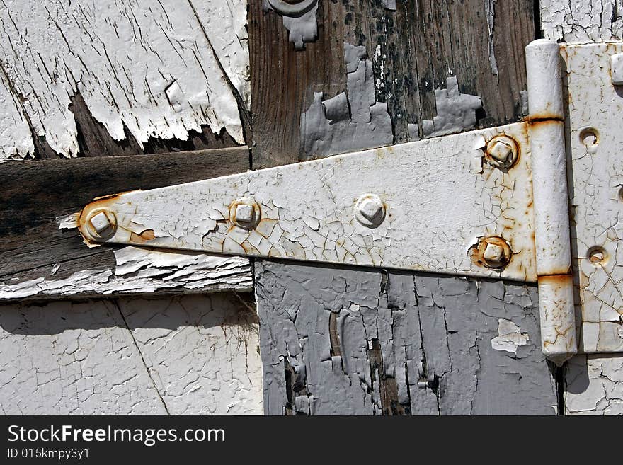 Texture shot of triangular-shaped hinge on old wooden door with weathered peeling grey and white paint. Texture shot of triangular-shaped hinge on old wooden door with weathered peeling grey and white paint