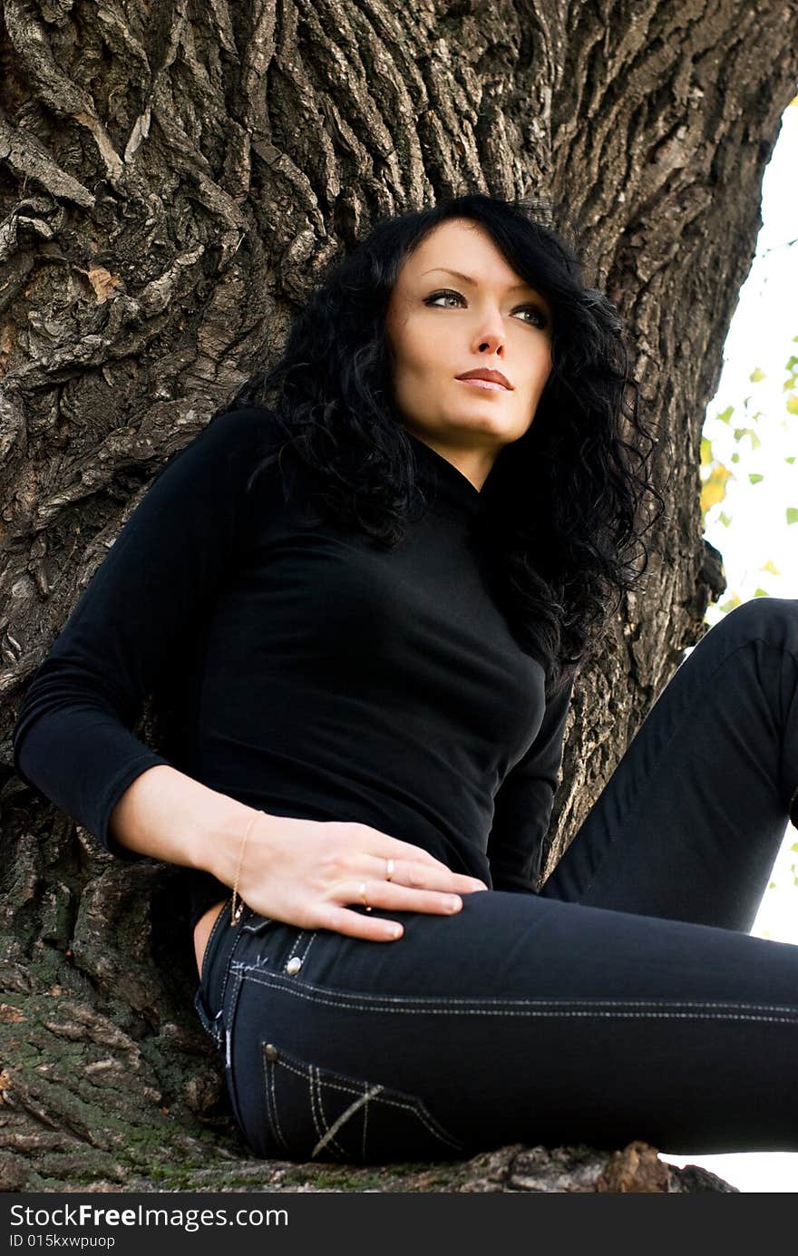 Beautiful thoughtful girl sitting on the tree in the park