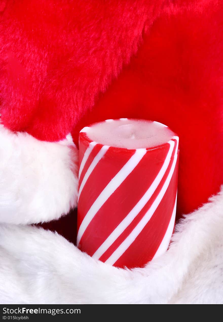 A striped candle nestled in a Santa's hat. A striped candle nestled in a Santa's hat