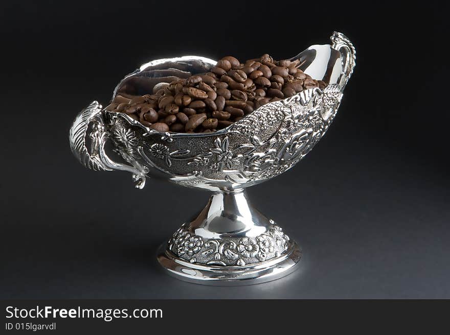 Coffee beans in a silver vase on a dark background. Coffee beans in a silver vase on a dark background