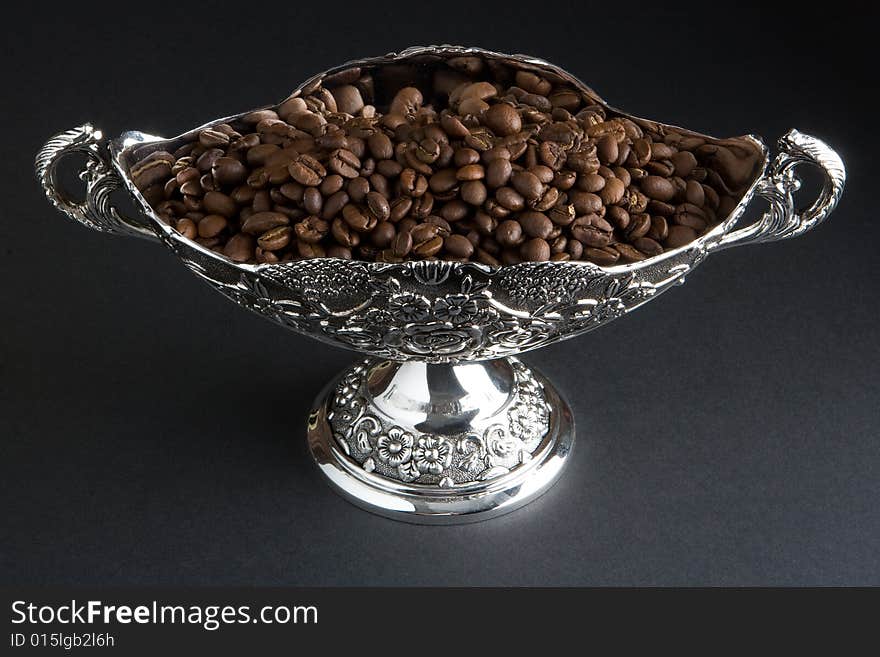 Coffee beans in a silver vase on a dark background