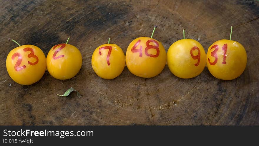 Line of yellow plums like lottery winning balls on wood surface