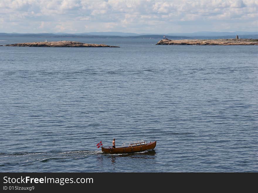 A man standing in his small wooden boat on his way in the fjord. A man standing in his small wooden boat on his way in the fjord