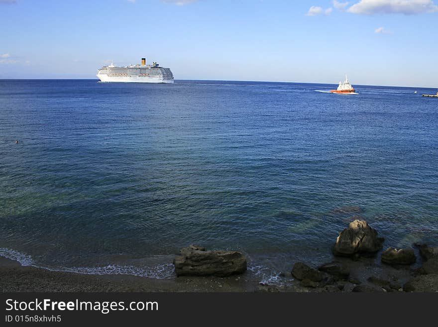 Cruise ship on the blue sea and the sky above with shore and rocks on the front . Cruise ship on the blue sea and the sky above with shore and rocks on the front