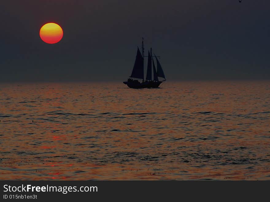 A old style sailing vessel sailing past a setting sun on Lake Michigan. A old style sailing vessel sailing past a setting sun on Lake Michigan