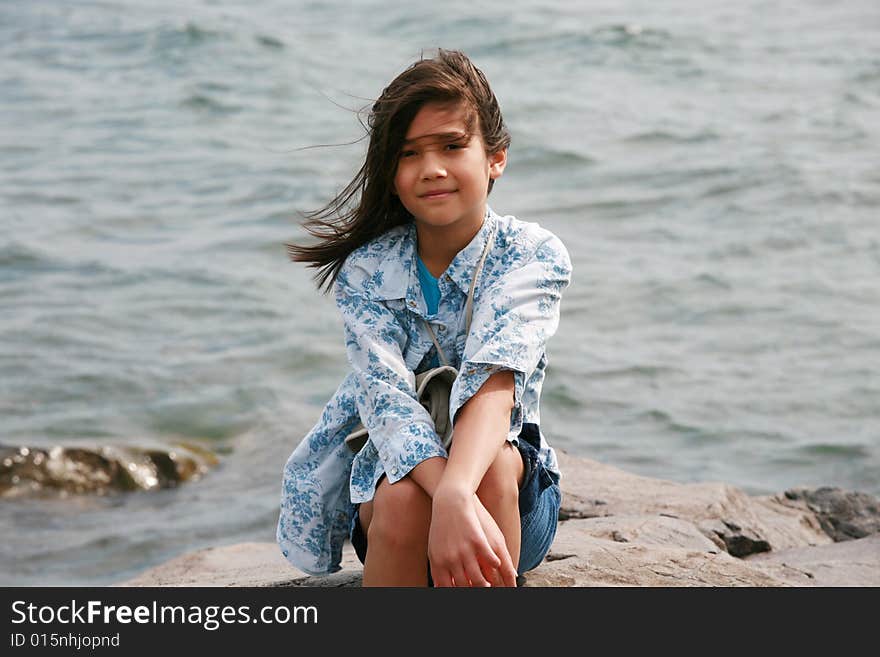 Nine year old girl sitting by lake in summer. Part asian- Scandinavian background.