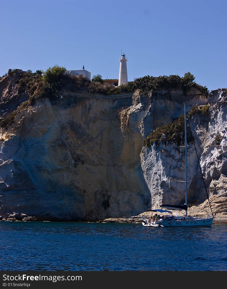 Lighthouse on steep mountain and sail yacht near Ponza island (Italy).