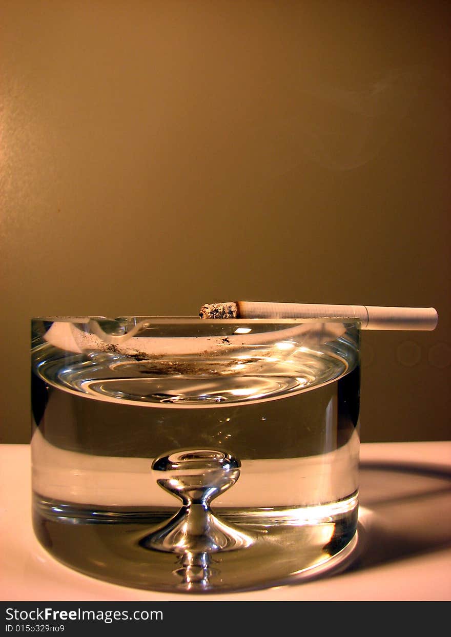 Cigarette on a big glass ash-tray.