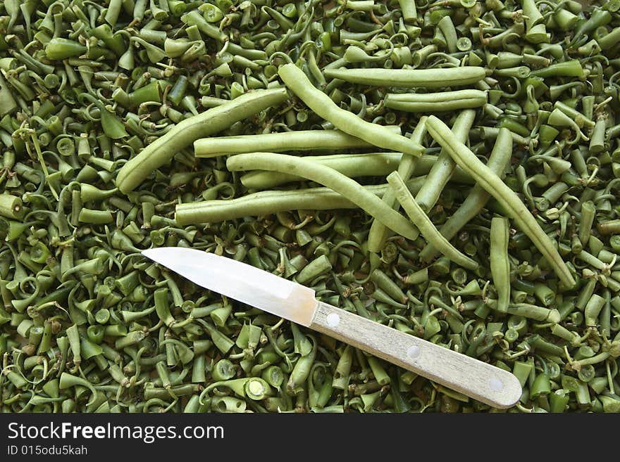 Green bush beans with ends removed on bed of bean ends - tops and tails- along with small vegetable knife. Green bush beans with ends removed on bed of bean ends - tops and tails- along with small vegetable knife.