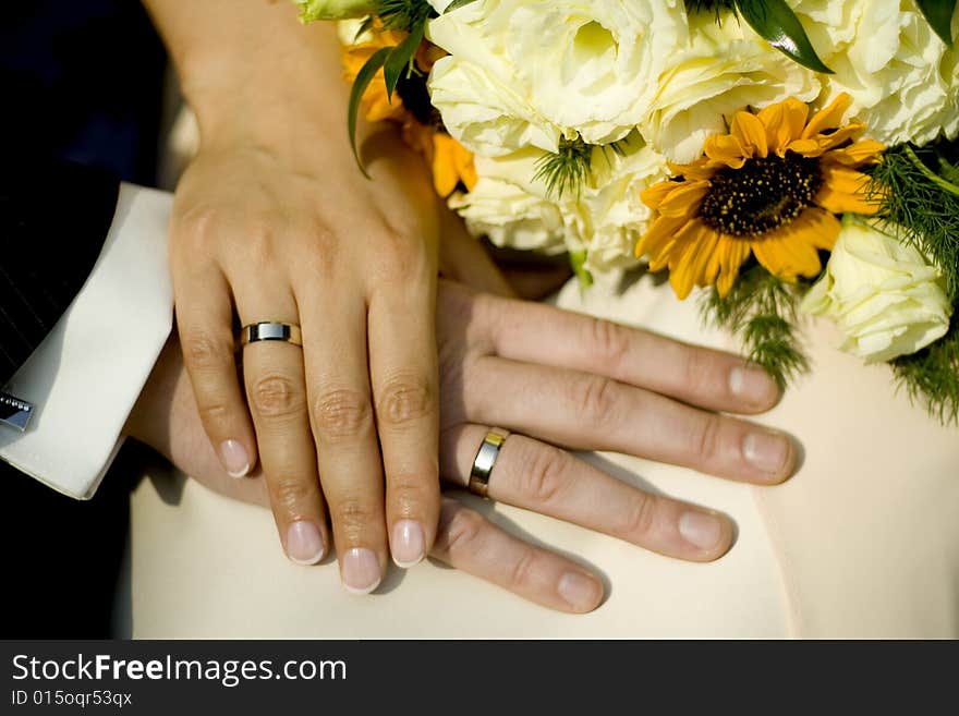 Holding hands of bride and groom with wedding bouquet in the background. Holding hands of bride and groom with wedding bouquet in the background