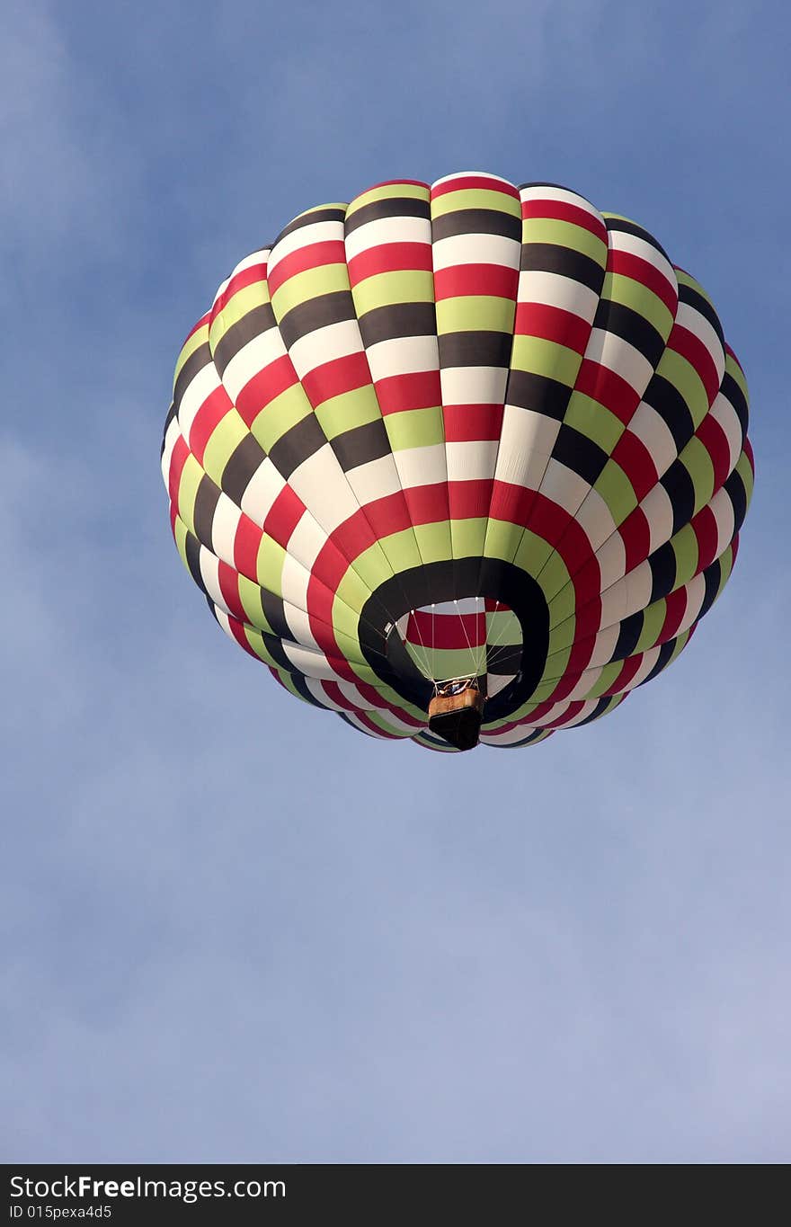 A multi-colored hot air balloon ascending into the clear blue sky