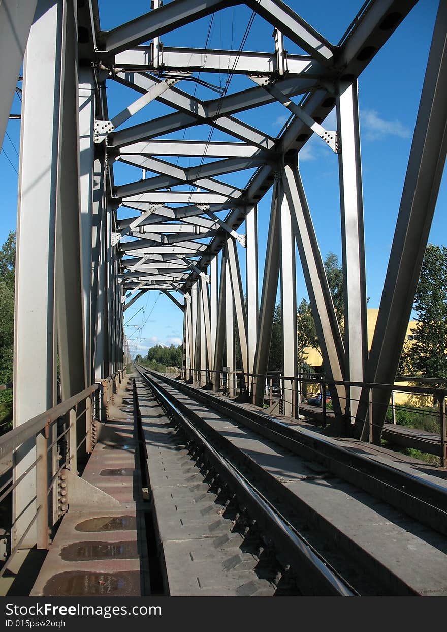 A running away railroad. A permanent way, a macadam, a sleepers and rails. A skylineand a overcast sky.railway bridge