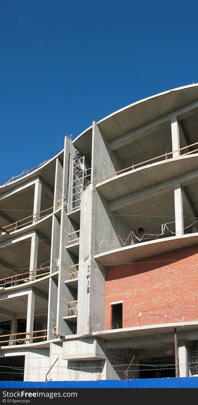 A building site, a hoisting crane and unfinished walls on the blue sky background.