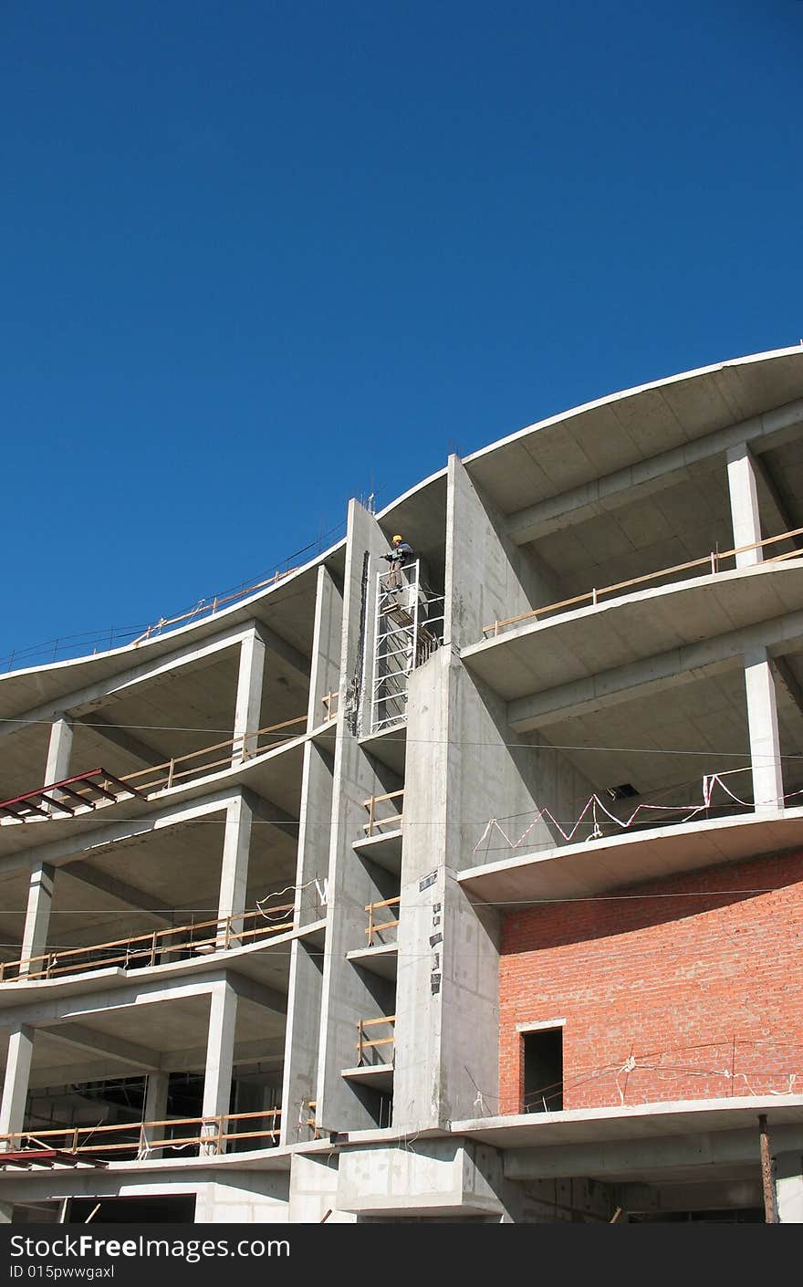 A building site, a hoisting crane and unfinished walls on the blue sky background.