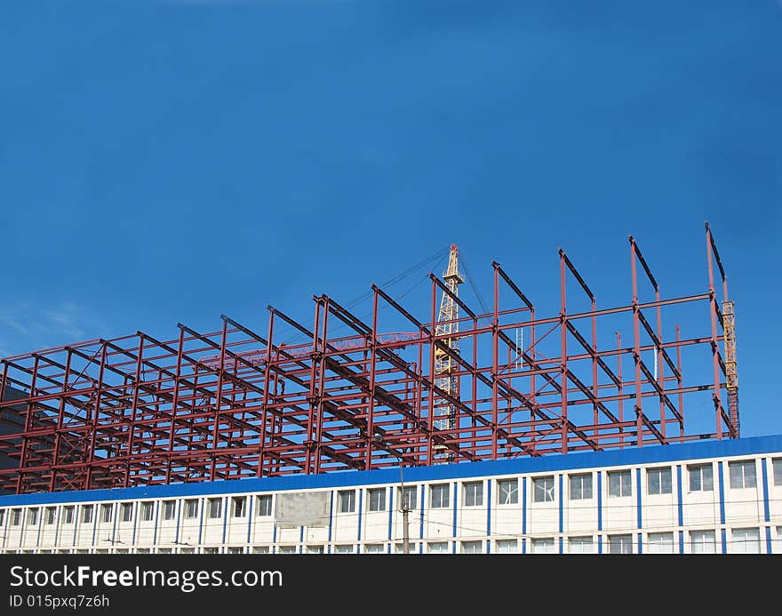 A building site, a hoisting crane and unfinished walls on the blue sky background.