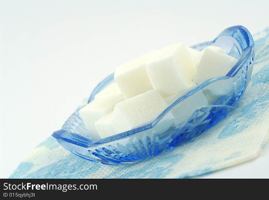 Sugar, blue glass saucer and napkin. On a white background. Sugar, blue glass saucer and napkin. On a white background.