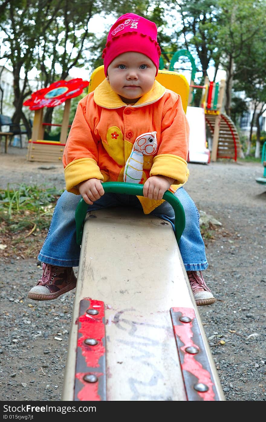 Pretty little girl with bright jacket sit on seesaw (teeter-totter). Pretty little girl with bright jacket sit on seesaw (teeter-totter).