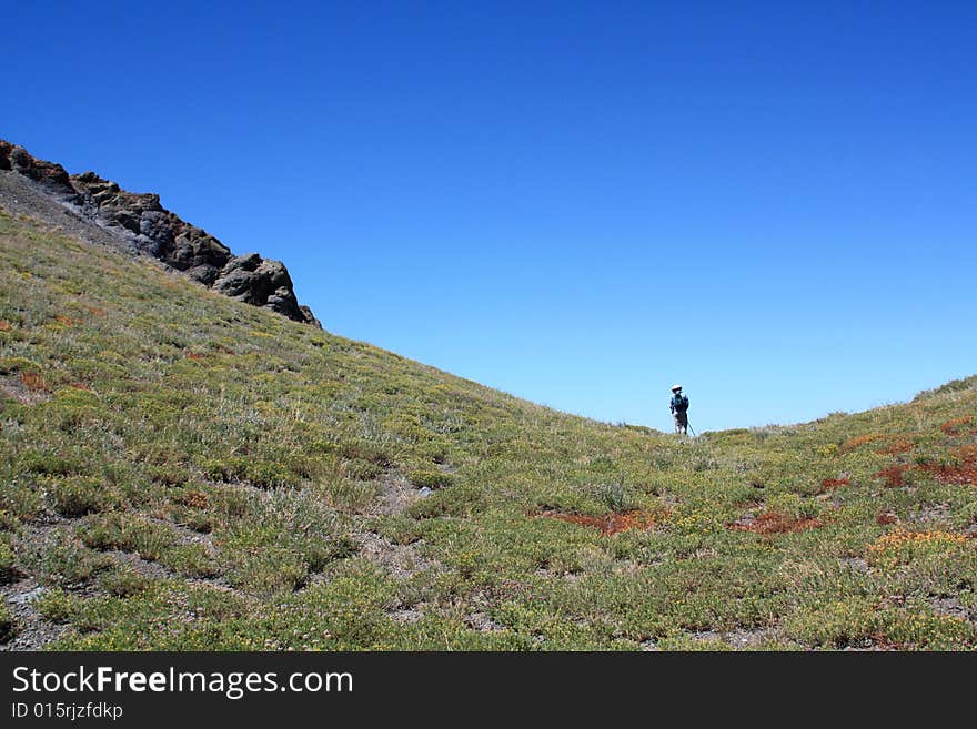 A lone hiker in a steep mountain saddle in the Sierra Nevada mountains.  California, U.S.A. A lone hiker in a steep mountain saddle in the Sierra Nevada mountains.  California, U.S.A