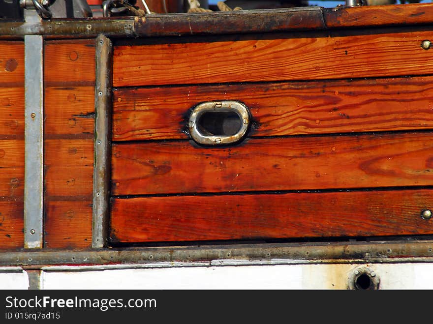 Detail of wooden planks and copper porthole on traditional wood schooner. Detail of wooden planks and copper porthole on traditional wood schooner.