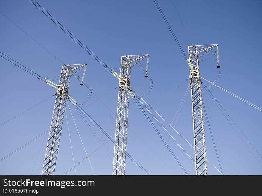 Three power lines with cables running in different directions against a blue sky. Three power lines with cables running in different directions against a blue sky.