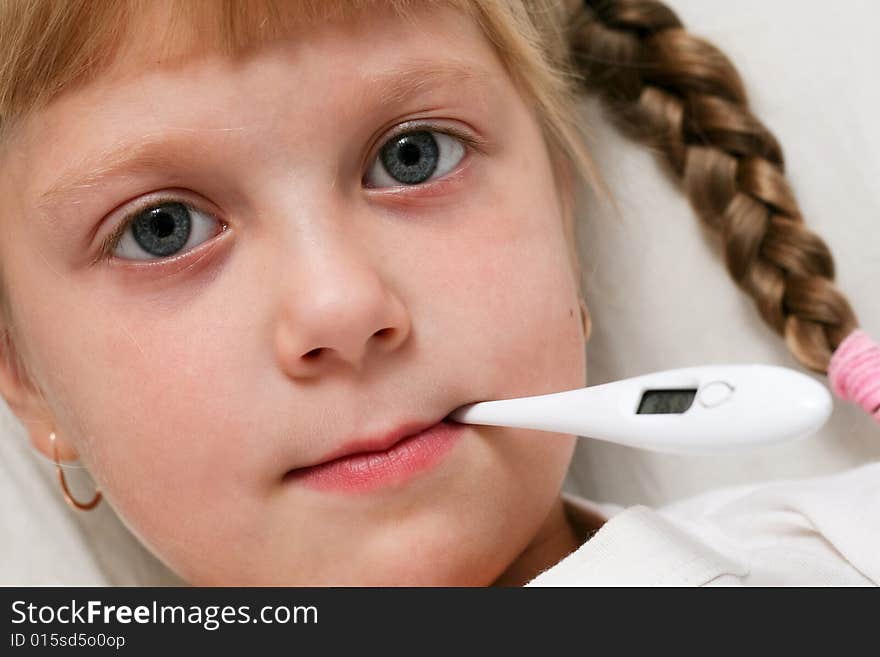 Child in bed under blanket with thermometer in mouth