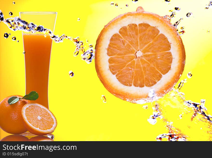 View of piece of orange getting splashed  and  glass of juice on back