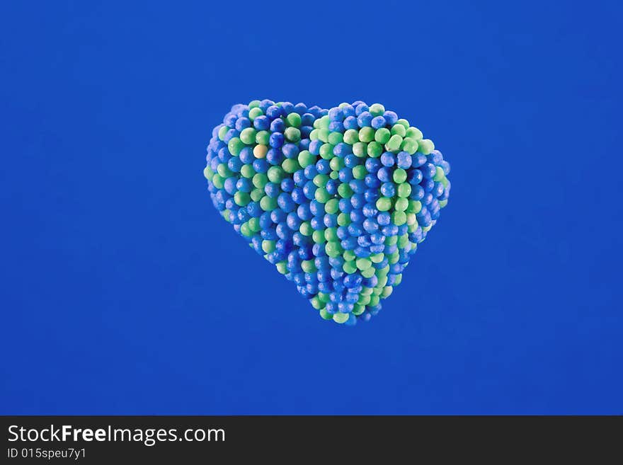 Candy heart encrusted with blue and green colored sugar balls, isolated on blue background