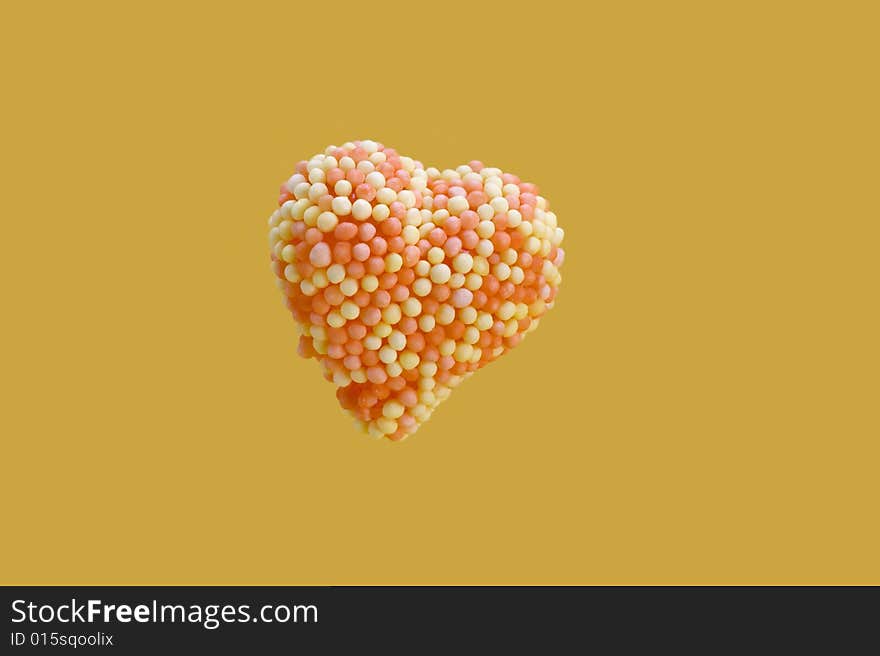 Candy heart encrusted with yellow and orange colored sugar, balls isolated on yellow background