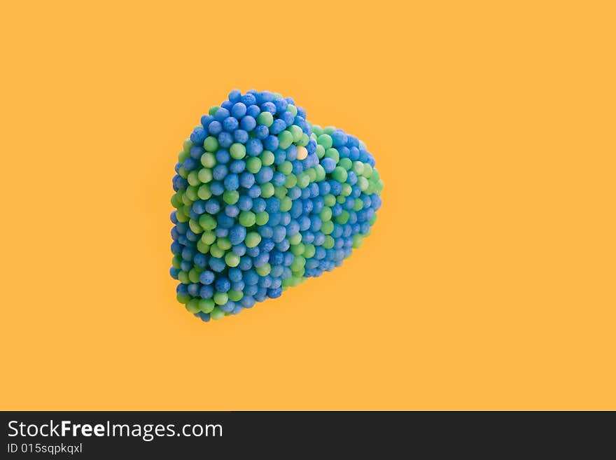 Candy heart encrusted with blue and green colored sugar balls isolated on yellow background