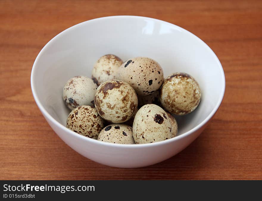 Quail eggs in a bowl on a wooden surface