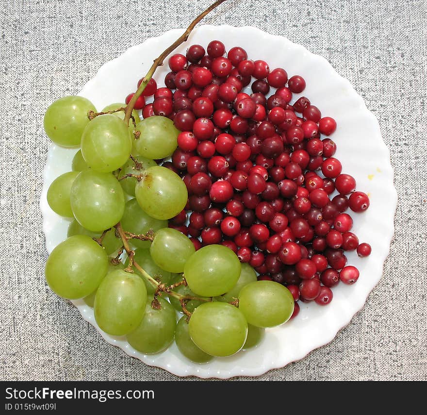 The autumn still life. Green grape, cranberries and helenium on the white  plate.